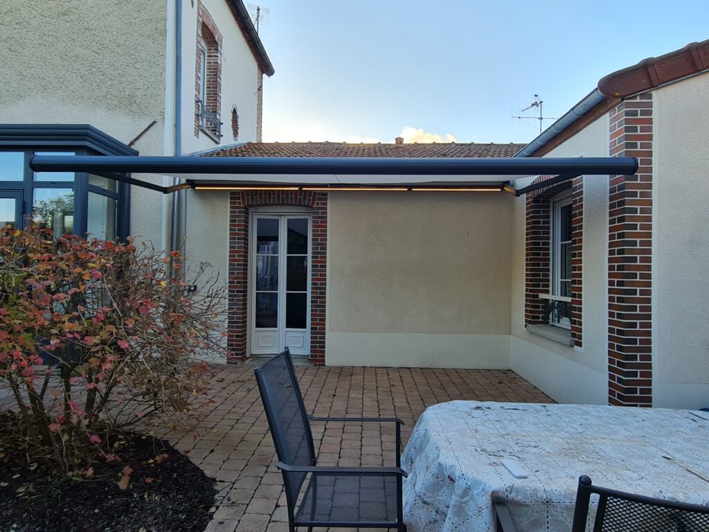 Store Félicia ouvert avec éclairage LED intégré – armature gris anthracite, toile blanche.