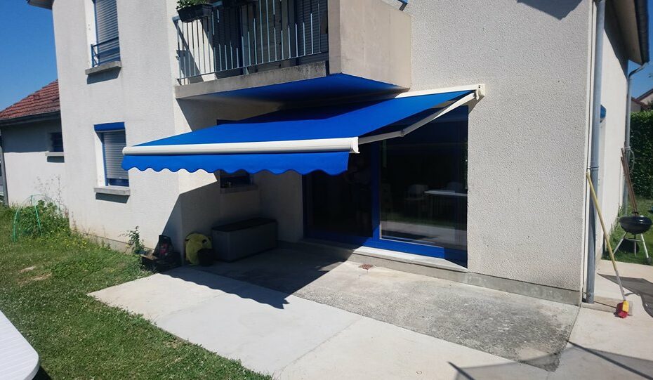 Store banne Fétuna ouvert sur terrasse, armature aluminium blanc et toile acrylique bleu unie avec lambrequin “vague”, pose sur mesure