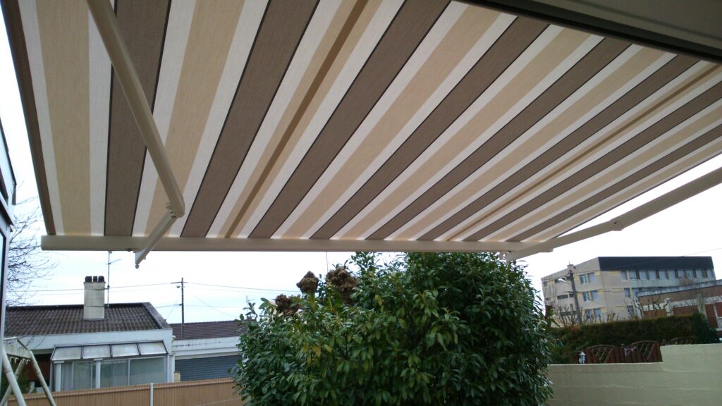 Store banne Horizon ouvert, vue en angle de la terrasse, installation professionnelle et toile beige rayée