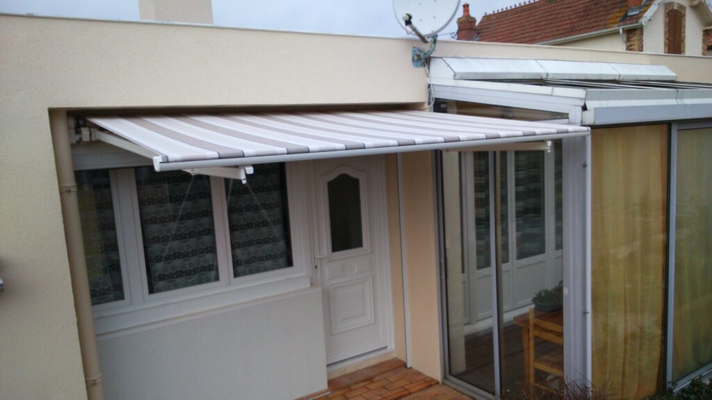 Store banne Horizon ouvert sur terrasse, armature blanche et toile acrylique beige rayée, pose sur mesure