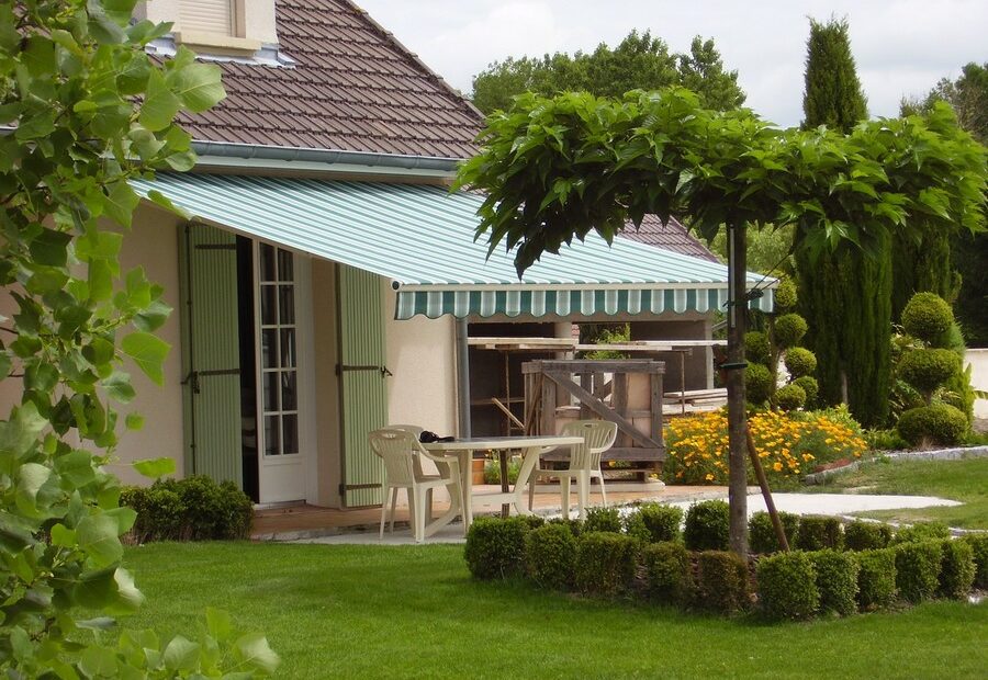 Store banne New Sumba 180 ouvert sur terrasse, armature aluminium blanc et toile acrylique verte rayée avec lambrequin “vague”, pose sur mesure
