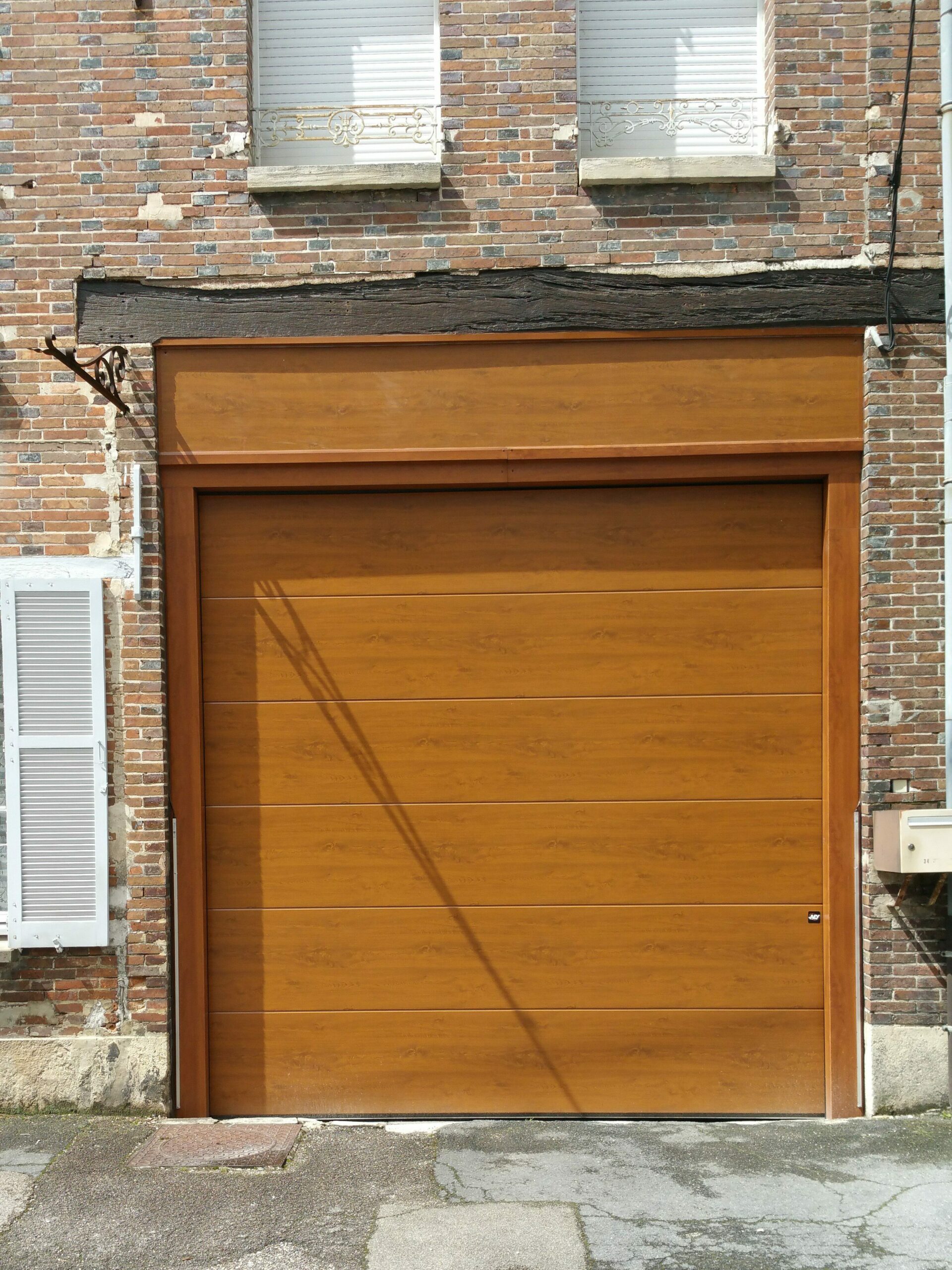 Porte de garage sectionnelle coloris chêne doré avec faux linteau installation sur mesure