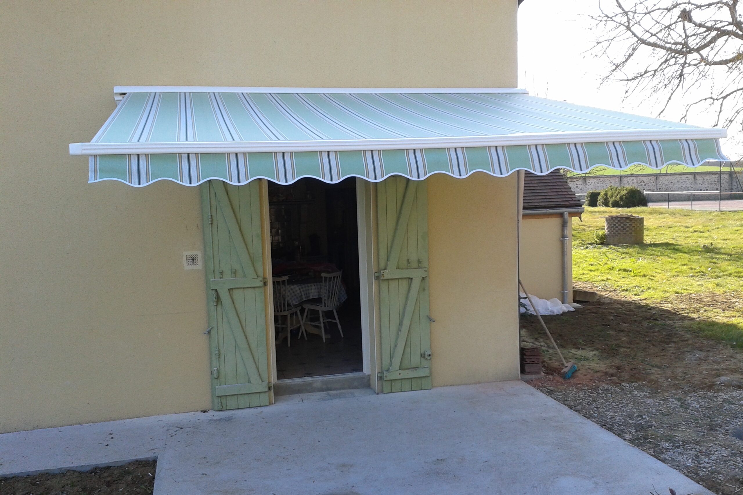 Store de terrasse Franciaflex Figari déployé avec toile rayée vert pâle